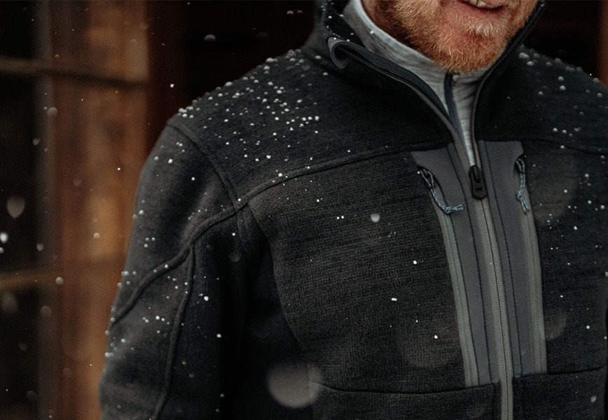 A man wearing Aktivator® Fleece Full Zip in front of a wooden cabin in snow