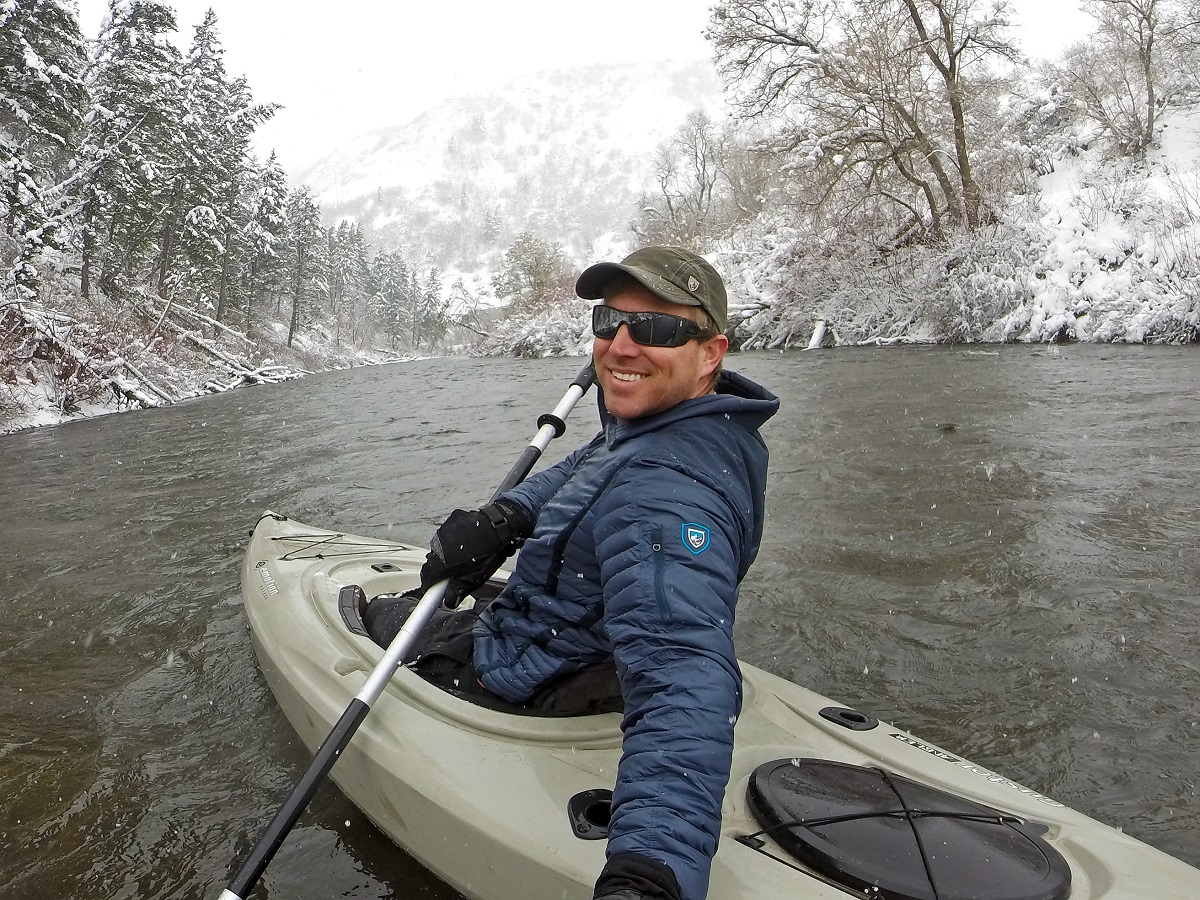 A man kayaking in the winter taking a selfie - dressed in KUHL men's winter kayaking outerwear