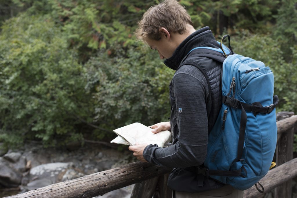 A man in KUHL jacket standing on a wooden bridge looking at a map.