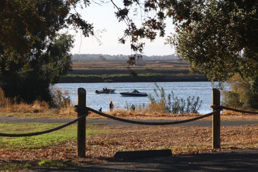 fence in front of brown and white ground with boats on water in background