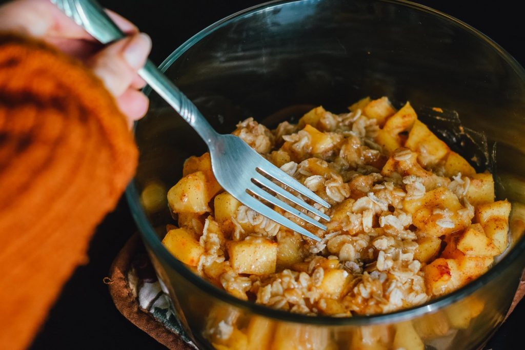 person holding fork in bowl with oats and sliced apple