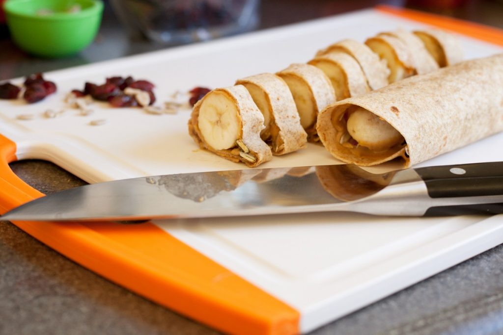 two bananas wrapped in tortilla next to knife