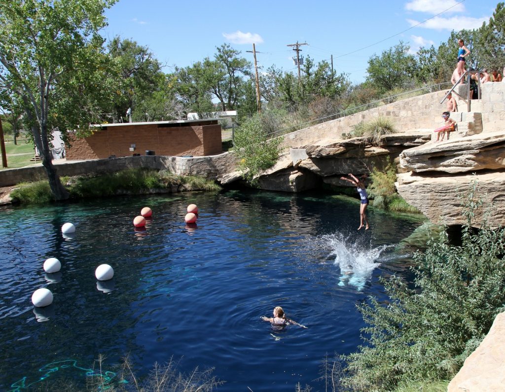 people swimming in body of water next to a cliff