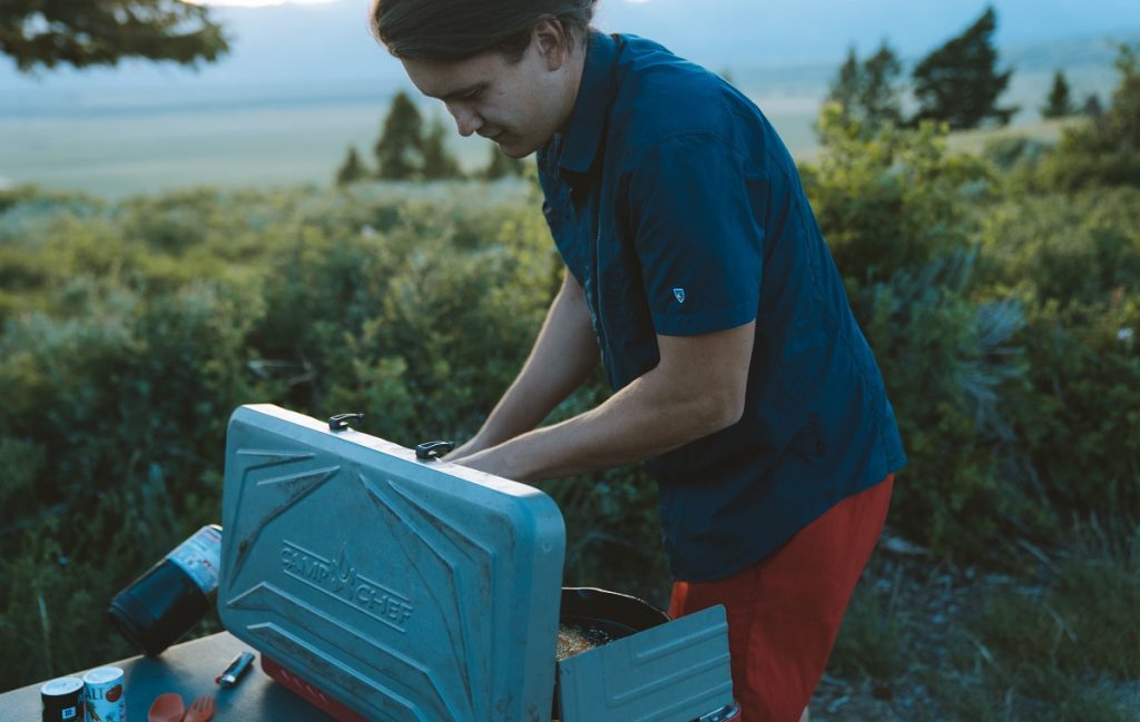 man in KÜHL short sleeve shirt cooking on portable stove