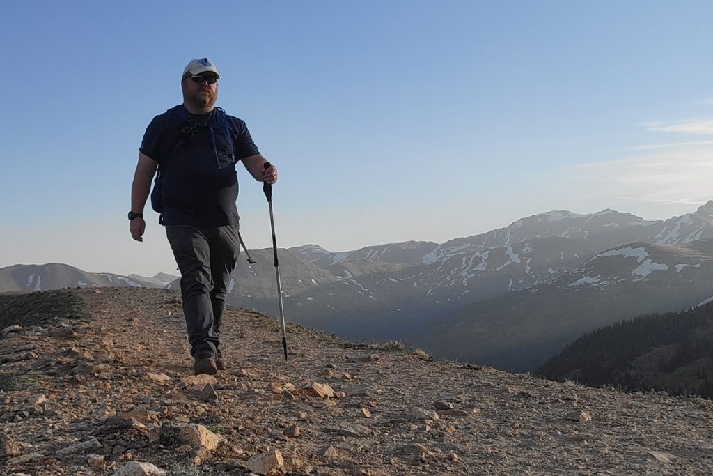 man in KÜHL pants and shirt hiking with a trekking pole during daytime